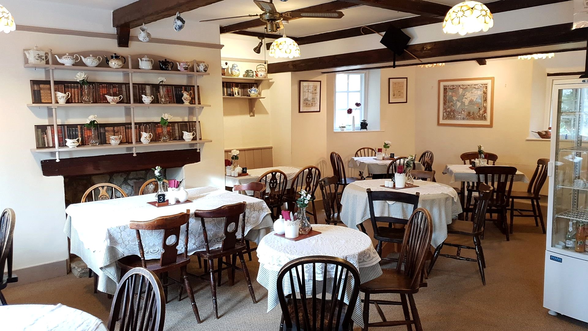 The tea room inside: round tables laid with white cloths, dark wooden chairs, a beamed ceiling and a dresser lined with teapots and cups