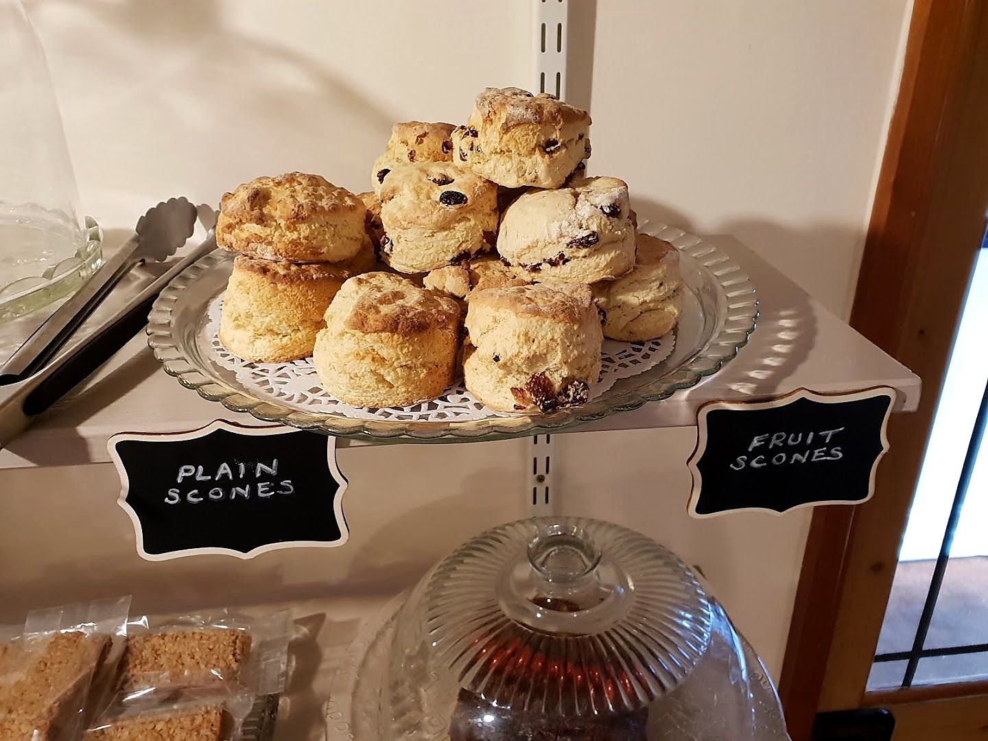 A glass cake stand piled with golden scones, with two small slate labels in chalk reading Plain scones and Fruit scones